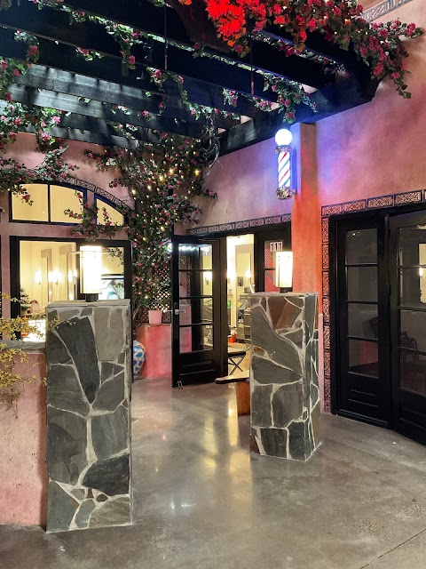 Terracotta courtyard entrance of El Patio Barber Lounge with stone pillars, barber pole and flowering pergola